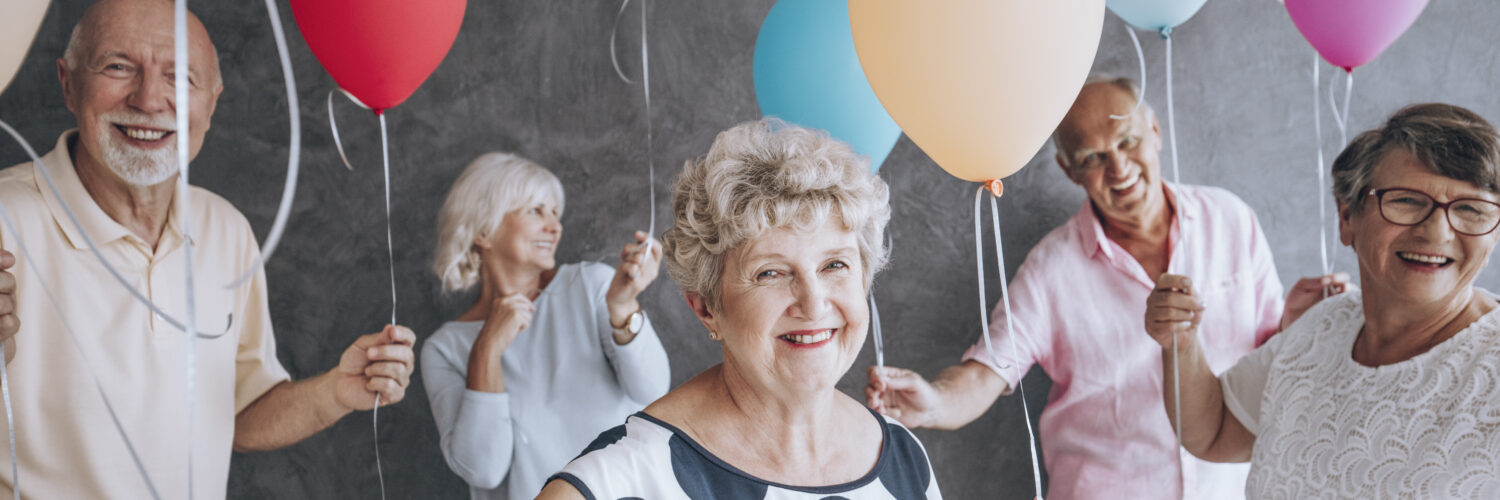 Group of older adults smiling and celebrating with balloons, symbolising joy, connection, and quality of life with Azure Care, through their home & live in care in Medway and Kent